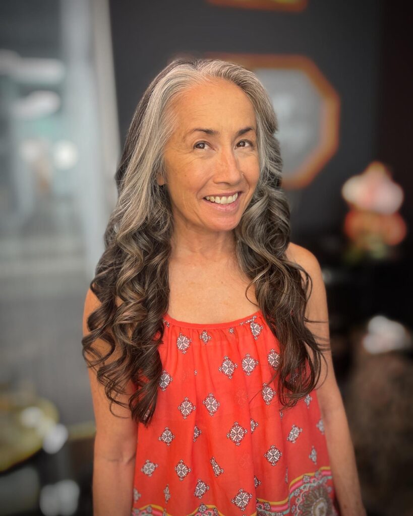 A woman with very long salt-and-pepper hair styled in polished cascading ringlets from mid-length to the ends.