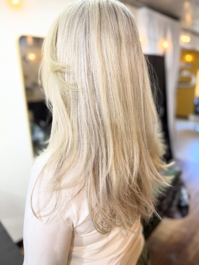 A woman with long, straight, creamy blonde hair featuring soft, feathery layers at the ends.