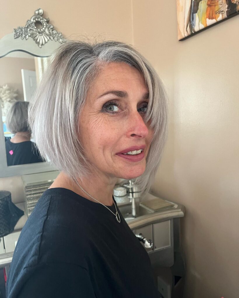 A woman over 50 with a short, modern asymmetrical bob haircut in a striking natural silver and grey color.