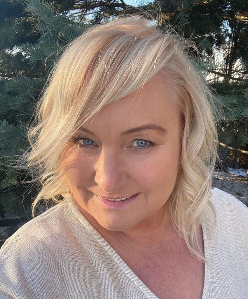 A woman with shoulder-length champagne-blonde hair styled in soft waves with a side-swept fringe.