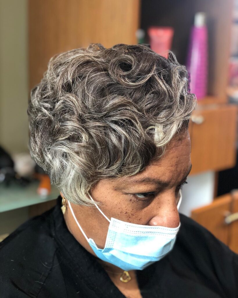 A close-up side view of a woman with a short salt-and-pepper hairstyle styled in elegant and sculpted finger waves.