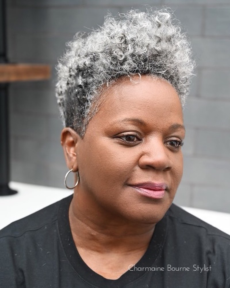 A woman with a short, tapered natural hairstyle featuring a voluminous silver curly top and dark, closely cropped sides.