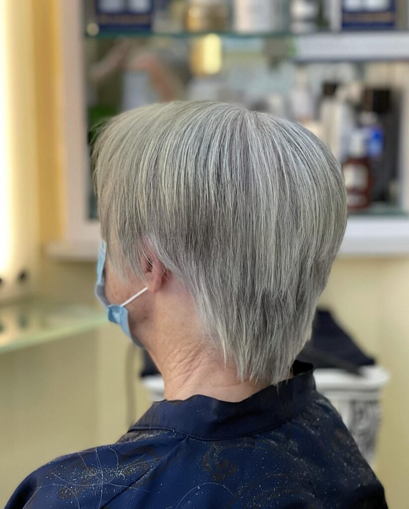 A back view of a woman with a sleek and straight tapered silver pixie cut.