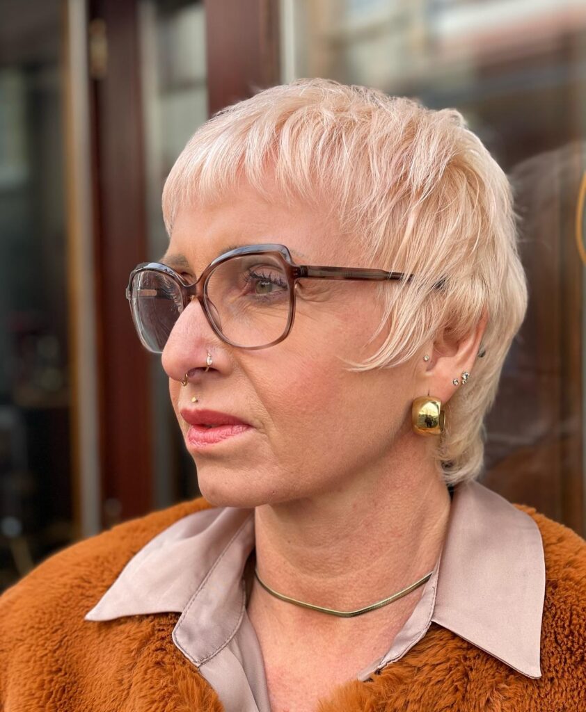 A woman with a textured peach-blonde pixie cut featuring choppy bangs and short layers.