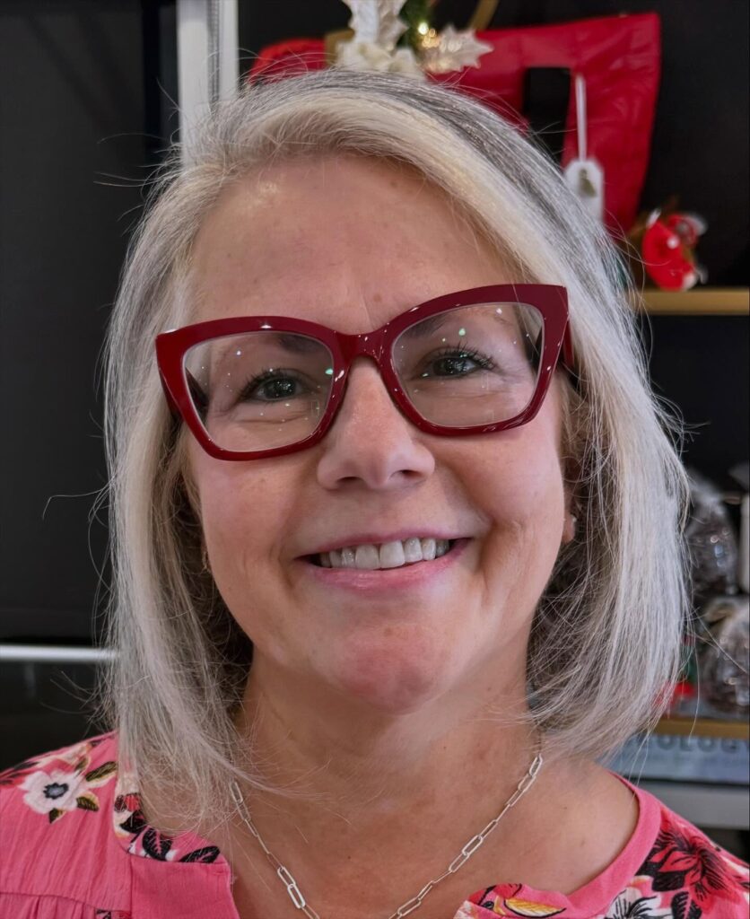 A smiling woman with red glasses and a classic chin-length silver bob with a soft side part.