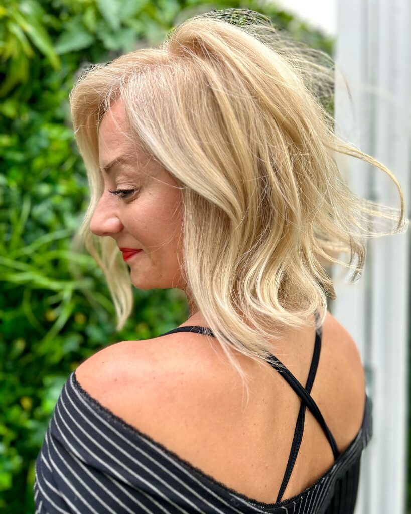 A woman viewed from the side with a wavy, shoulder-length champagne blonde lob and a breezy texture.