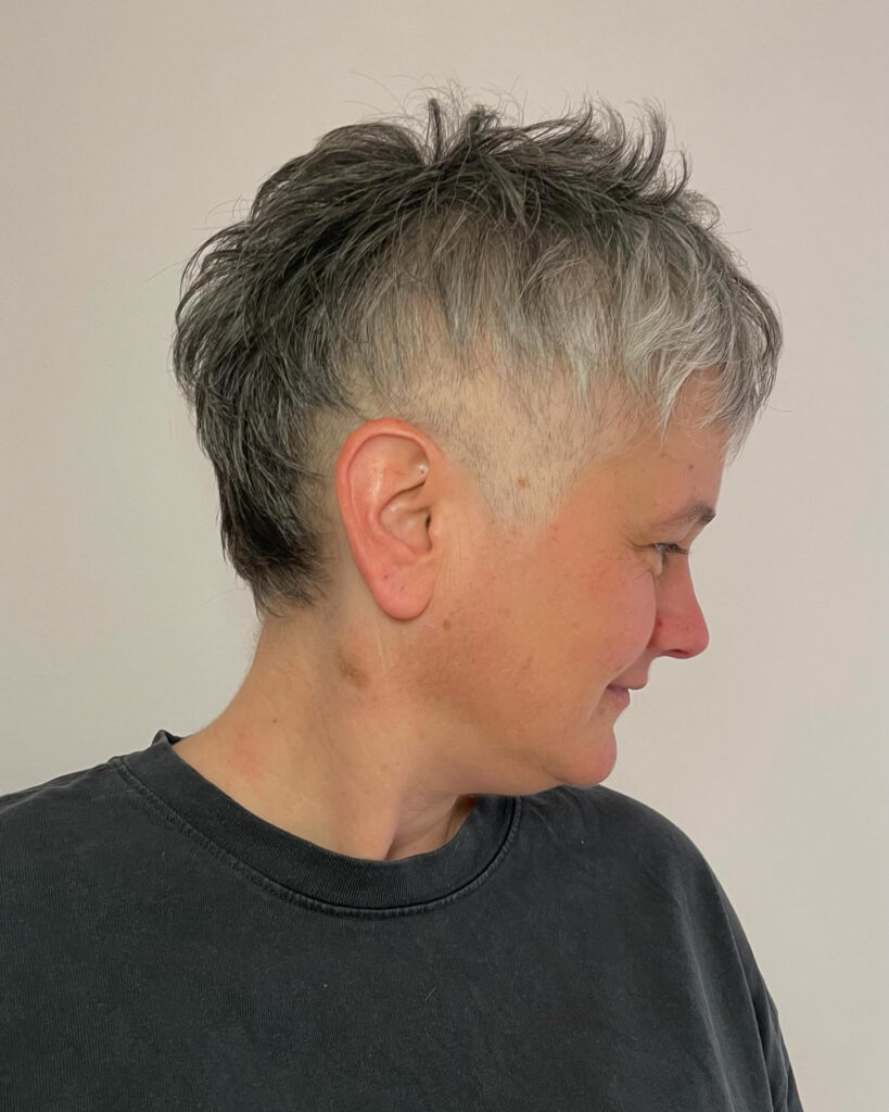 A side profile of a woman with a bold salt and pepper pixie cut featuring a visible undercut and textured layers on top.