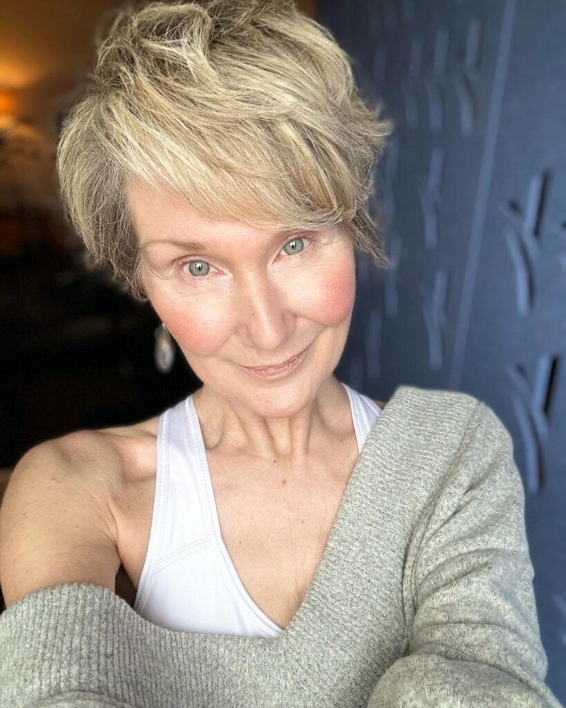 A woman over 50 with a voluminous wavy pixie cut in champagne blonde with textured side-swept bangs.