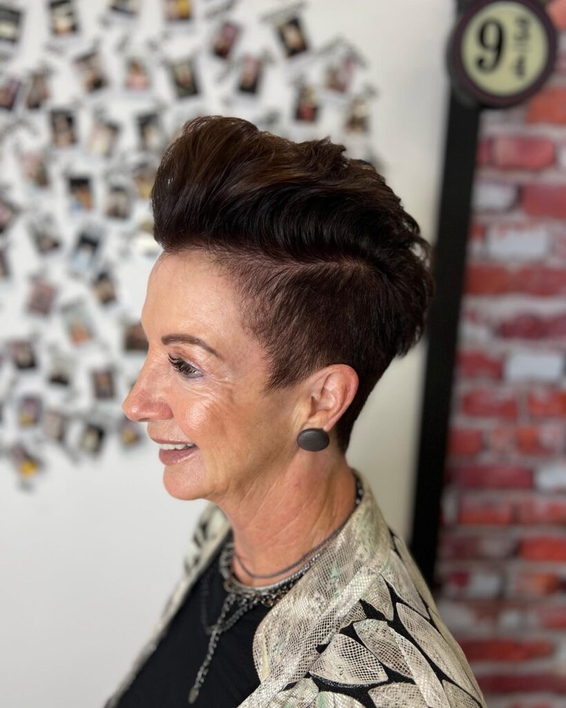 A woman over 50 with a dark brunette pompadour hairstyle featuring shaved sides and voluminous, swept-back length on top.