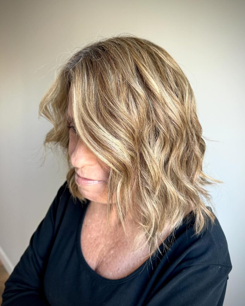 A woman over 50 with a shoulder-length sandy blonde lob featuring beachy waves and soft highlights.
