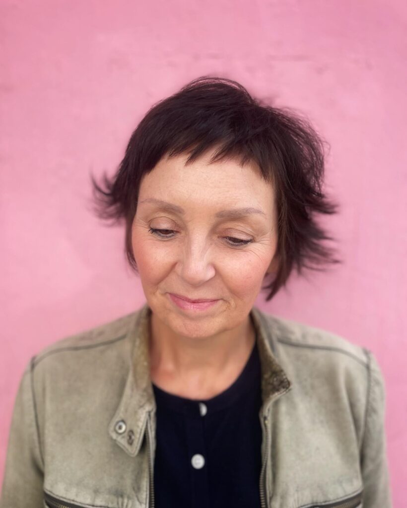 A woman over 50 with a dark espresso bixie cut featuring short micro bangs and feathery outward flipped ends.