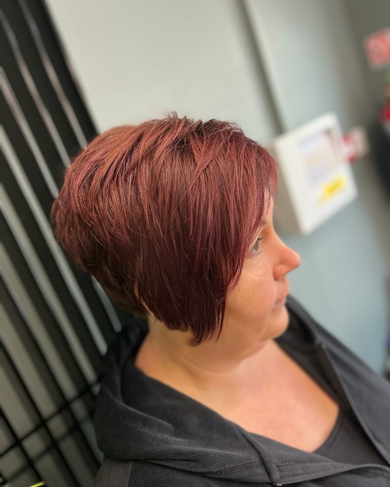 A woman over 50 with a vibrant burgundy bixie cut featuring asymmetrical layers and a side-swept fringe.