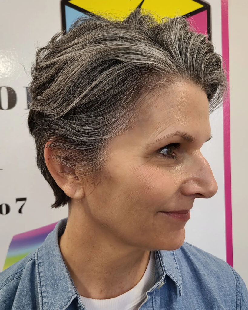 A woman over 50 with a textured salt and pepper pixie cut styled away from her face to show off silver highlights.