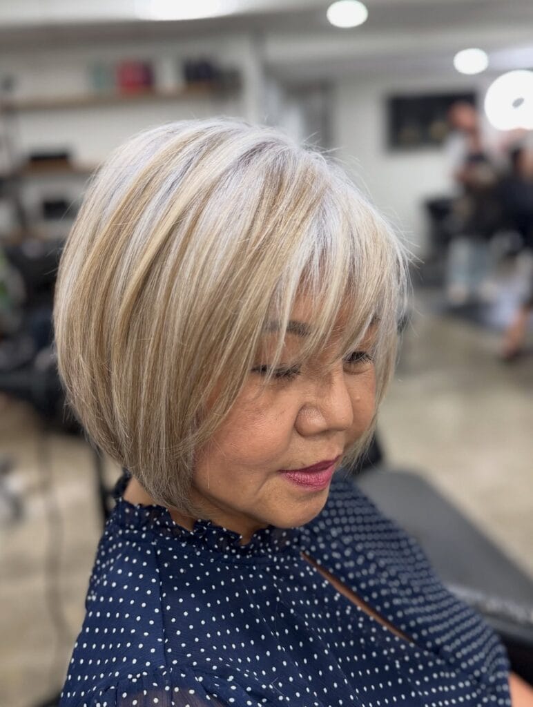 Layered blonde gray bob with wispy bangs and soft volume.