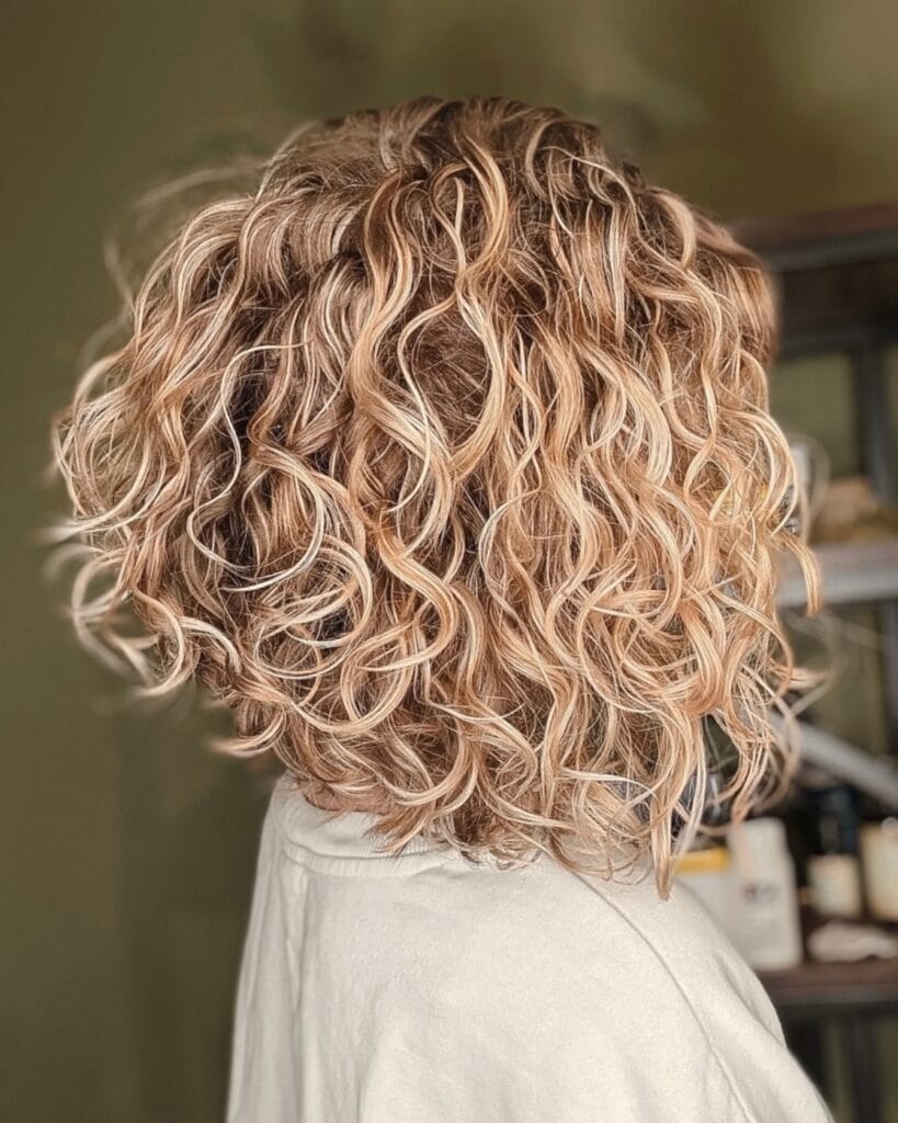 Curly inverted bob with voluminous layers and warm blonde tones.