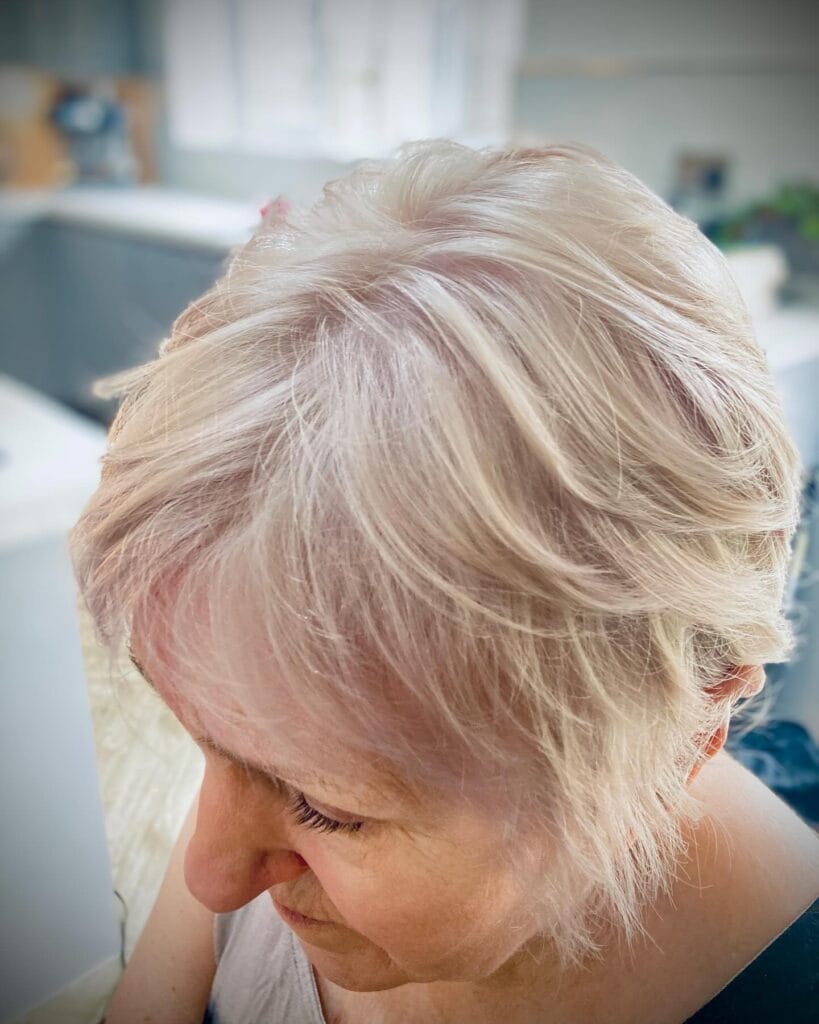 Short feathered pixie bob with soft layers, wispy fringe, and light blonde color.