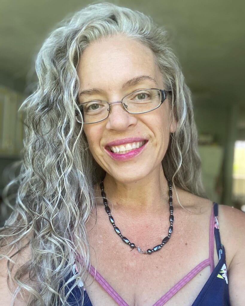 Long gray curly hair with a side part and loose texture.