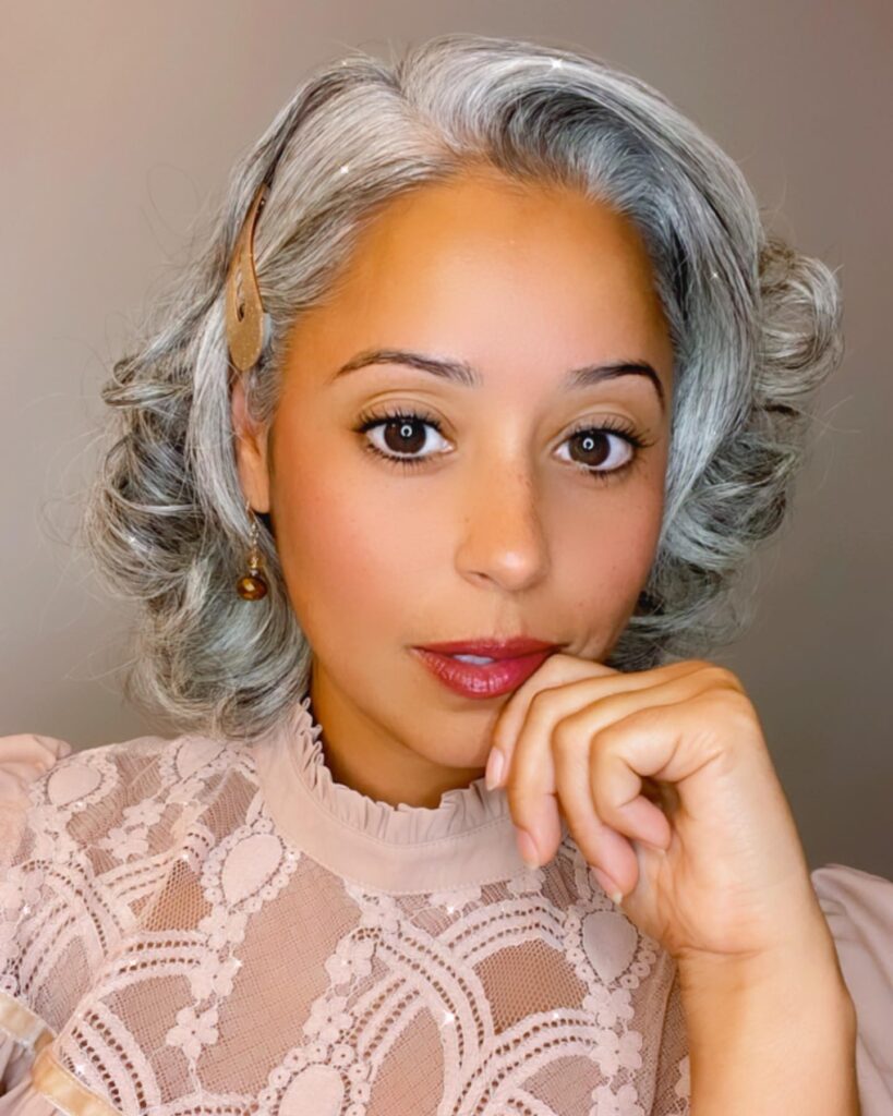 A woman with shoulder-length curly gray hair pinned to one side with a gold clip.
