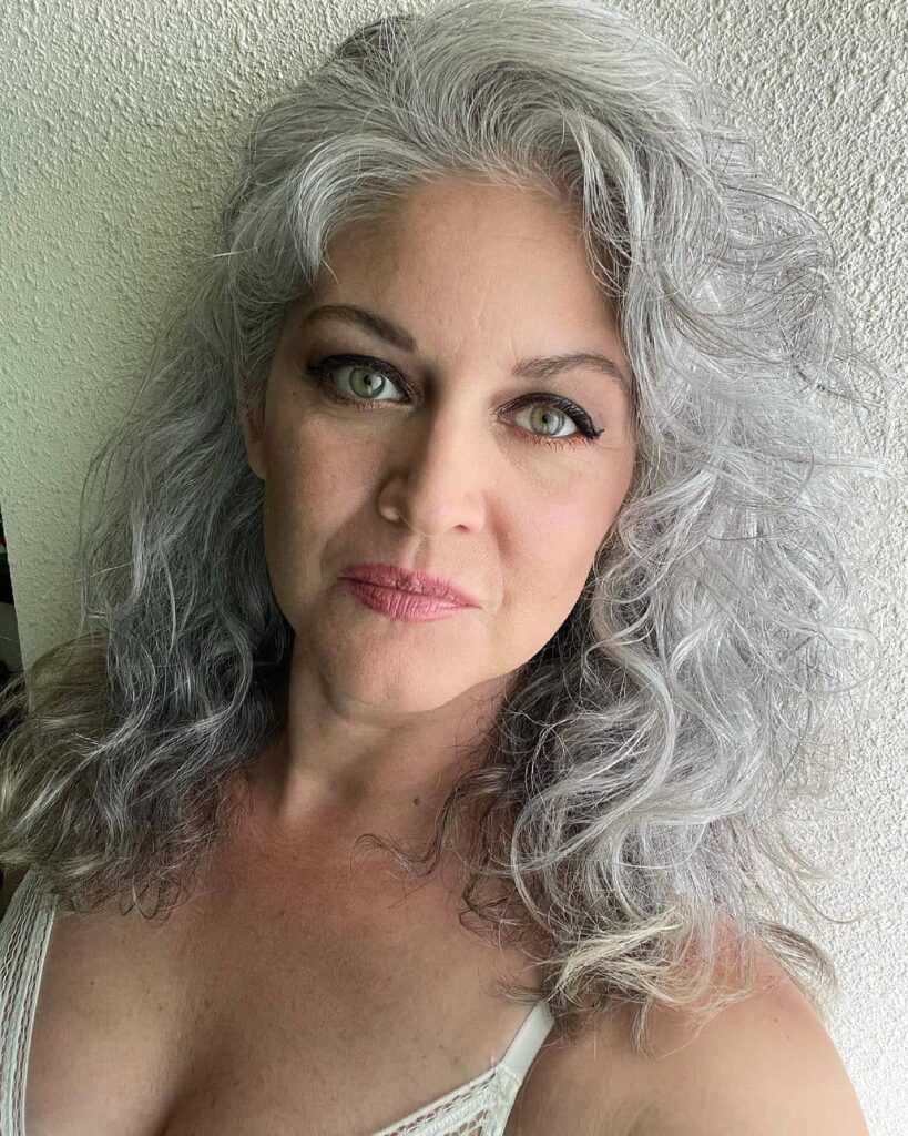A woman with long, wavy salt-and-pepper hair that falls past her shoulders in a layered style.