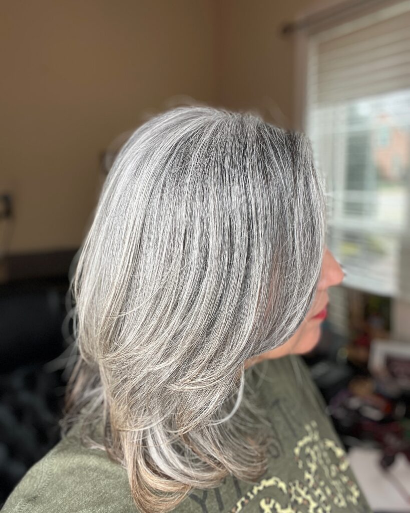 A side view of a woman with shoulder-length straight gray hair featuring soft layered ends.