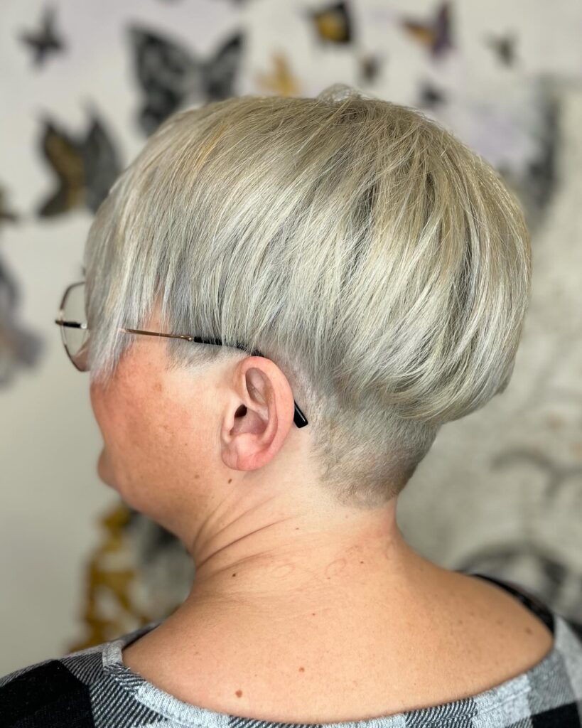 A woman with a rounded silver bob hairstyle featuring a short tapered undercut at the nape and smooth, voluminous layers.
