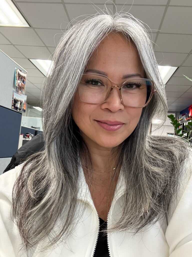 A woman with long layered straight hair in a mix of dark gray and bright silver tones.