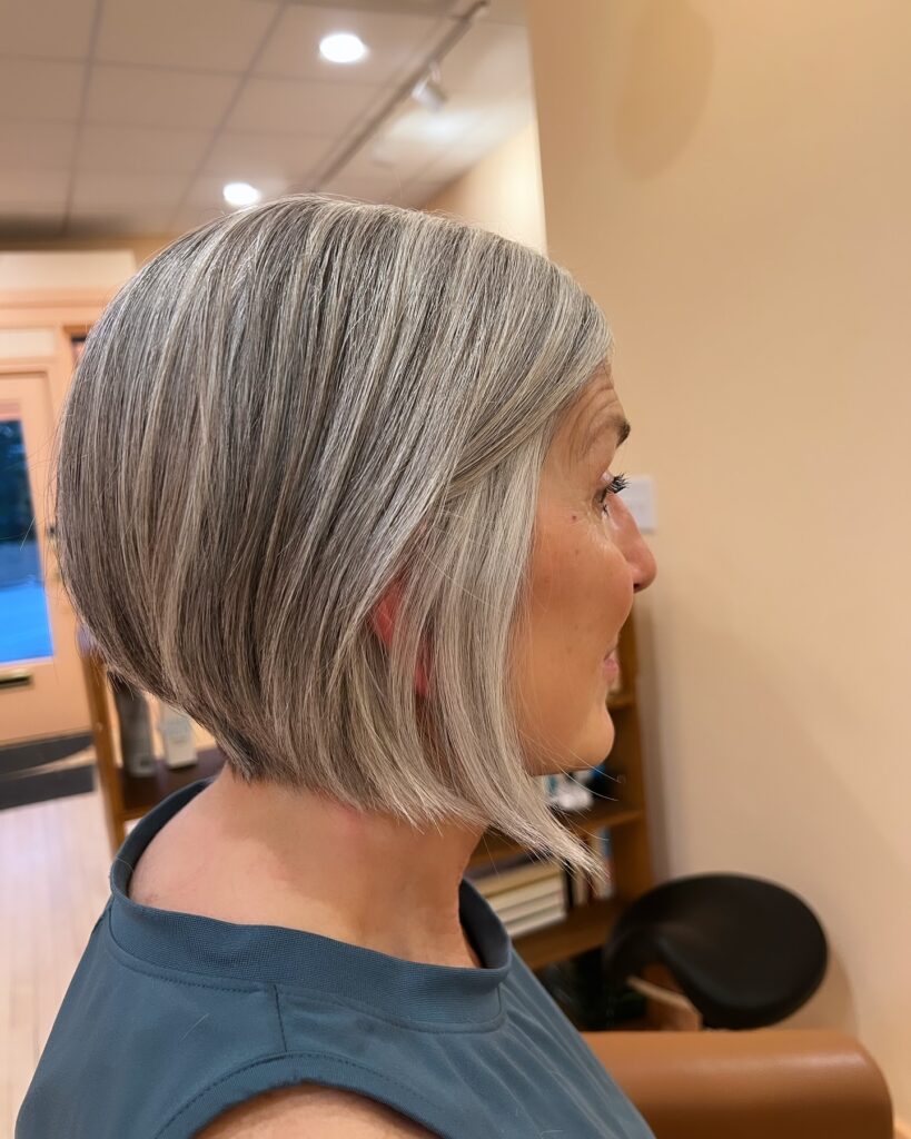 A side view of a woman with an angled, inverted silver bob that is shorter at the back and tapers into longer straight layers at the front.