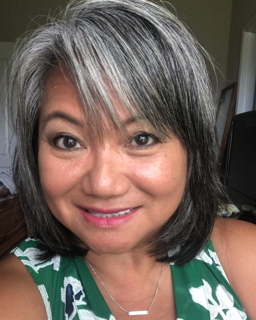 A woman with a chin-length salt-and-pepper bob featuring side-swept bangs and a blend of dark and silver-gray hair.
