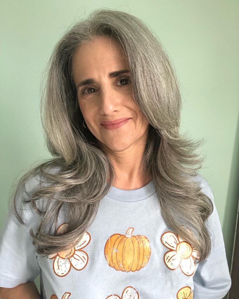 A woman with long gray hair featuring feathered layers flicked outward at the ends.