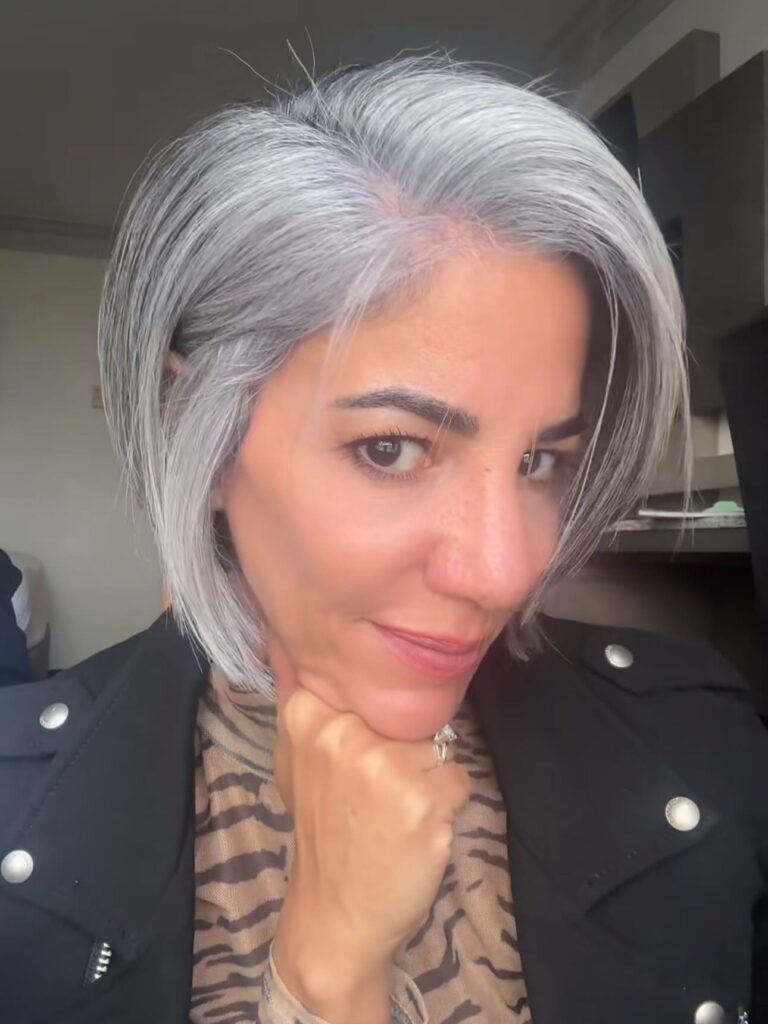 A woman with a sleek chin-length silver bob tucked behind one ear with a deep side part and a glossy straight finish.