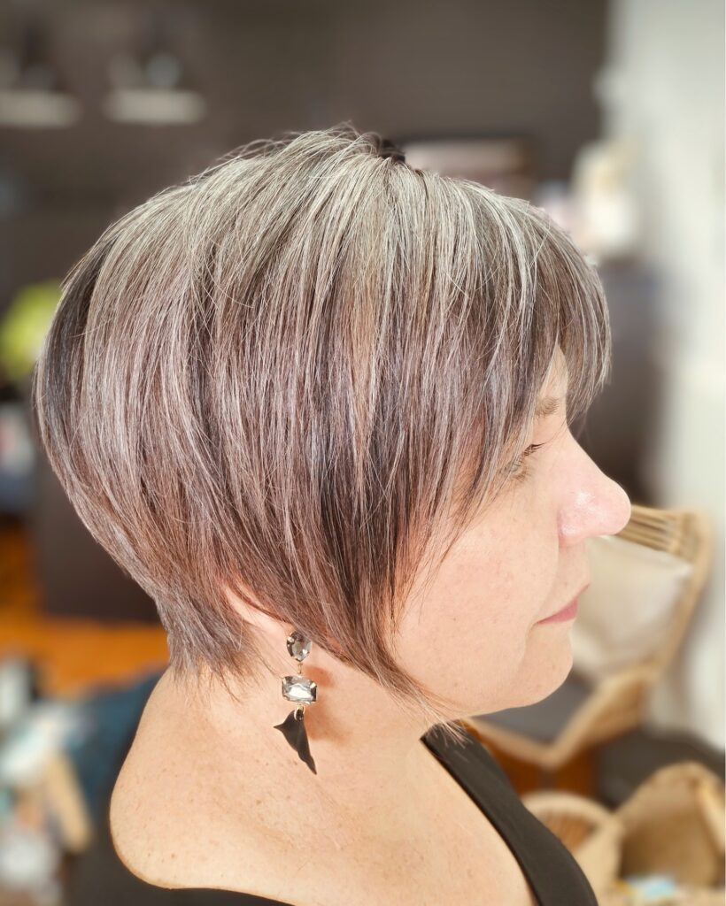 A woman viewed from the side with a short stacked pixie bob featuring silver and brown highlights.