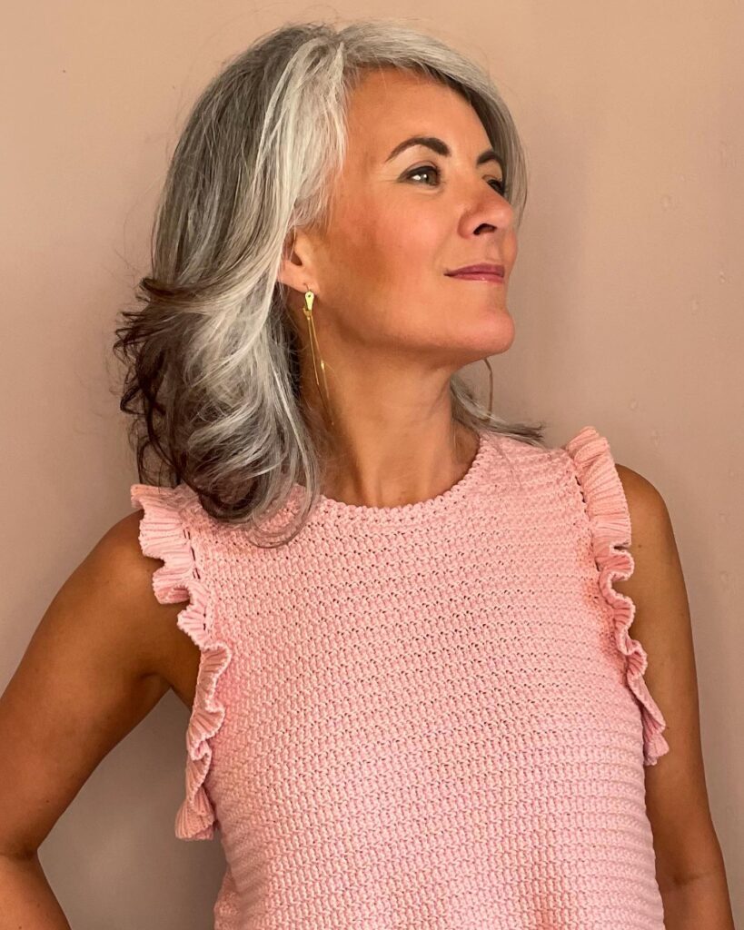 A woman with shoulder-length wavy hair featuring a dark gray base and bright silver highlights swept back to show off her profile.