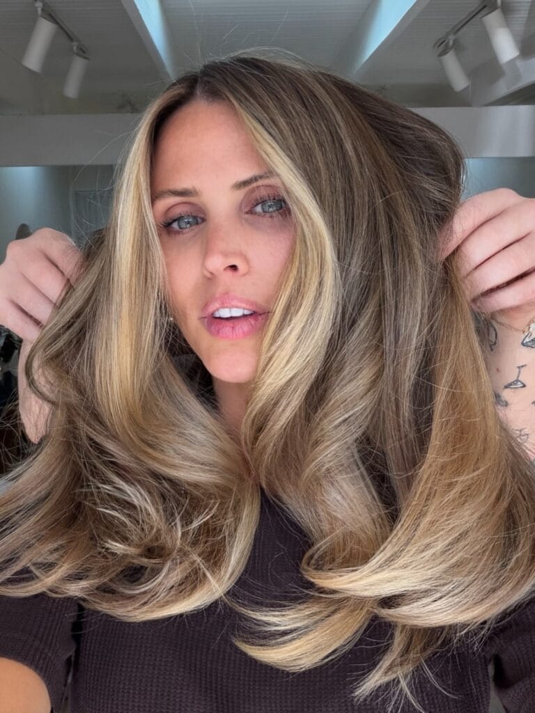 Long layered blonde hair with feathered waves and soft volume.