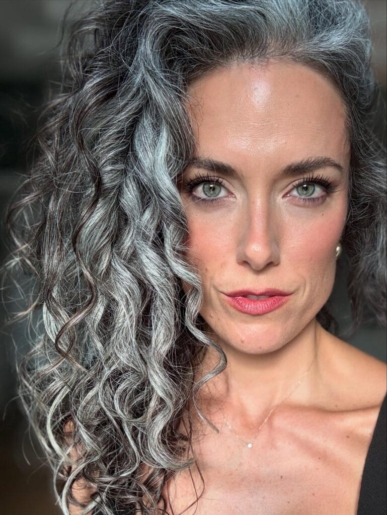 Long silver gray hair styled in dramatic side swept waves with defined curls.