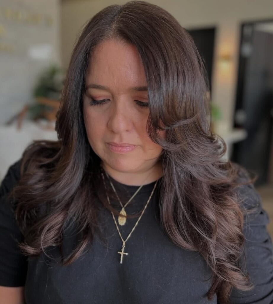 Long brunette layered hair with soft glossy waves and a smooth finish.