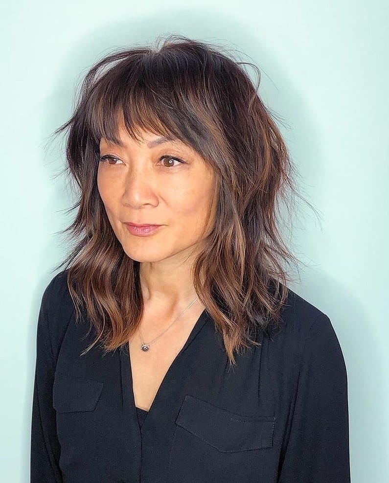Medium length shaggy layered hair with wispy bangs and a tousled texture.