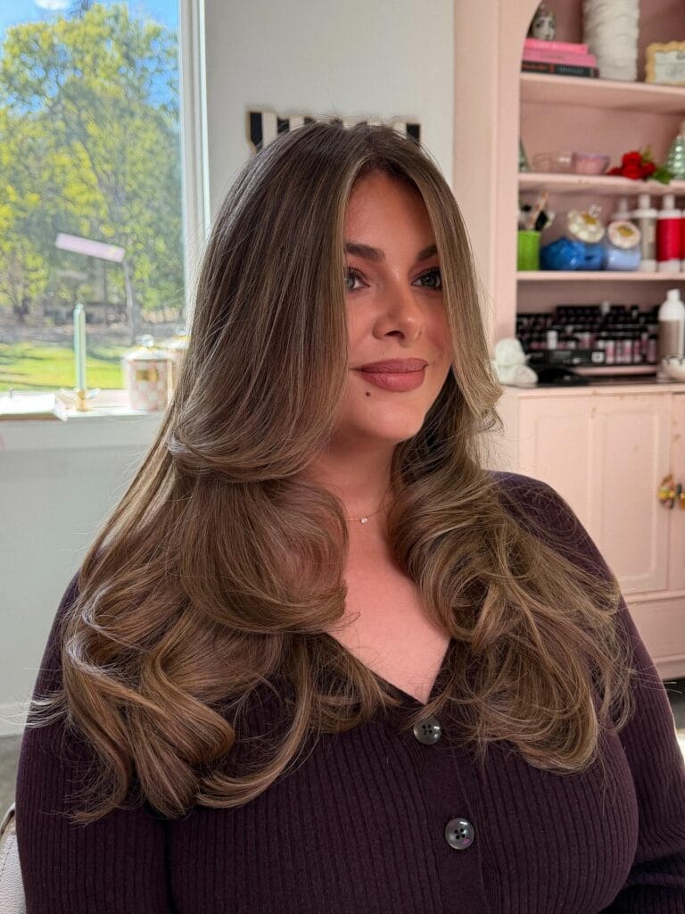 Long brunette layered hair with soft curls and voluminous body.