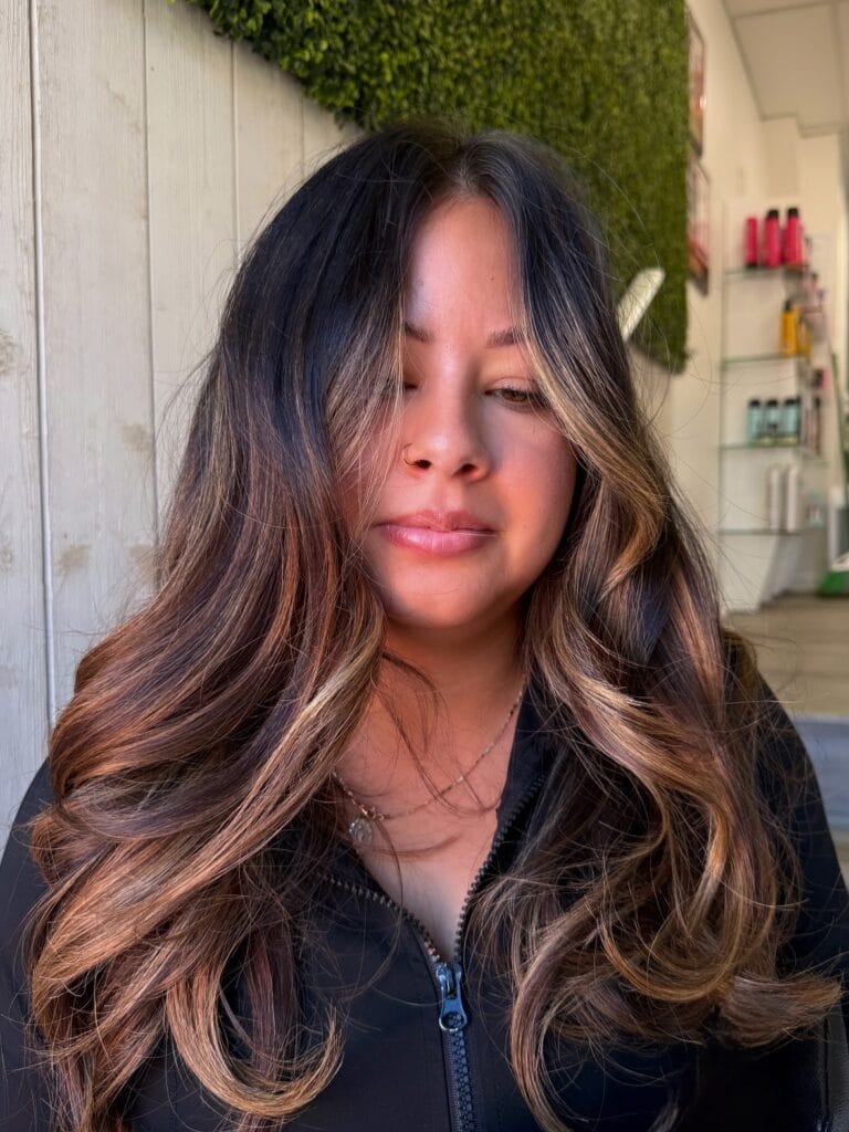 Long layered hair with soft waves and warm balayage highlights framing the face.