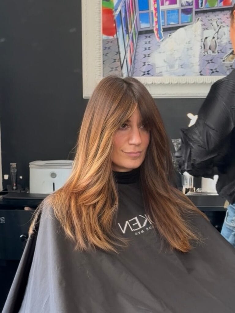 Long brunette layered hair with subtle face framing and a smooth finish.
