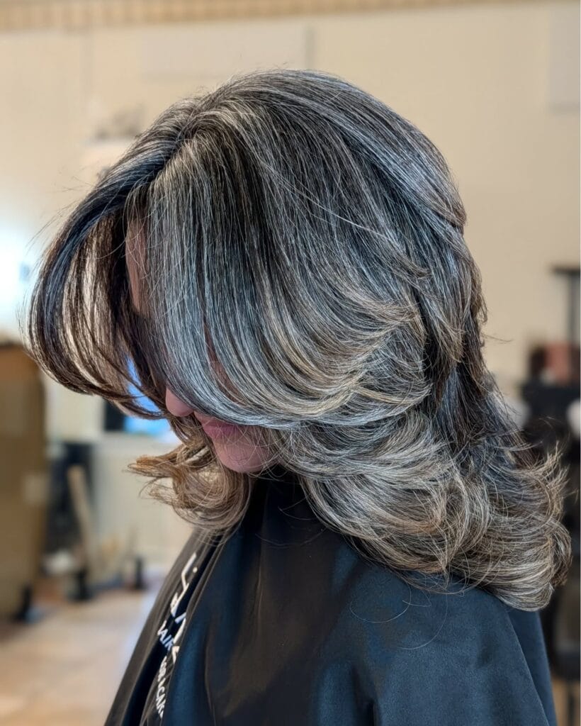 Medium length layered hair with feathered ends and a blend of silver and dark tones.