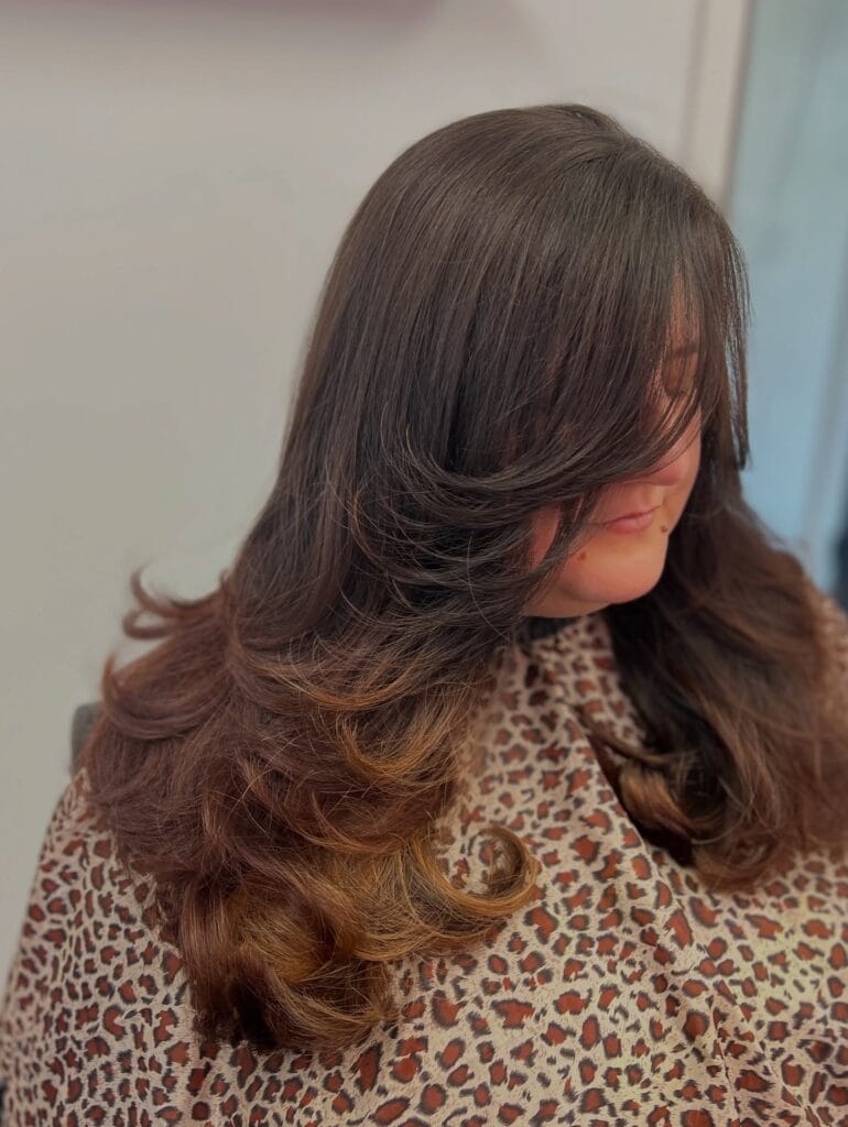 Long brunette layered hair with soft curls and voluminous, rounded ends.