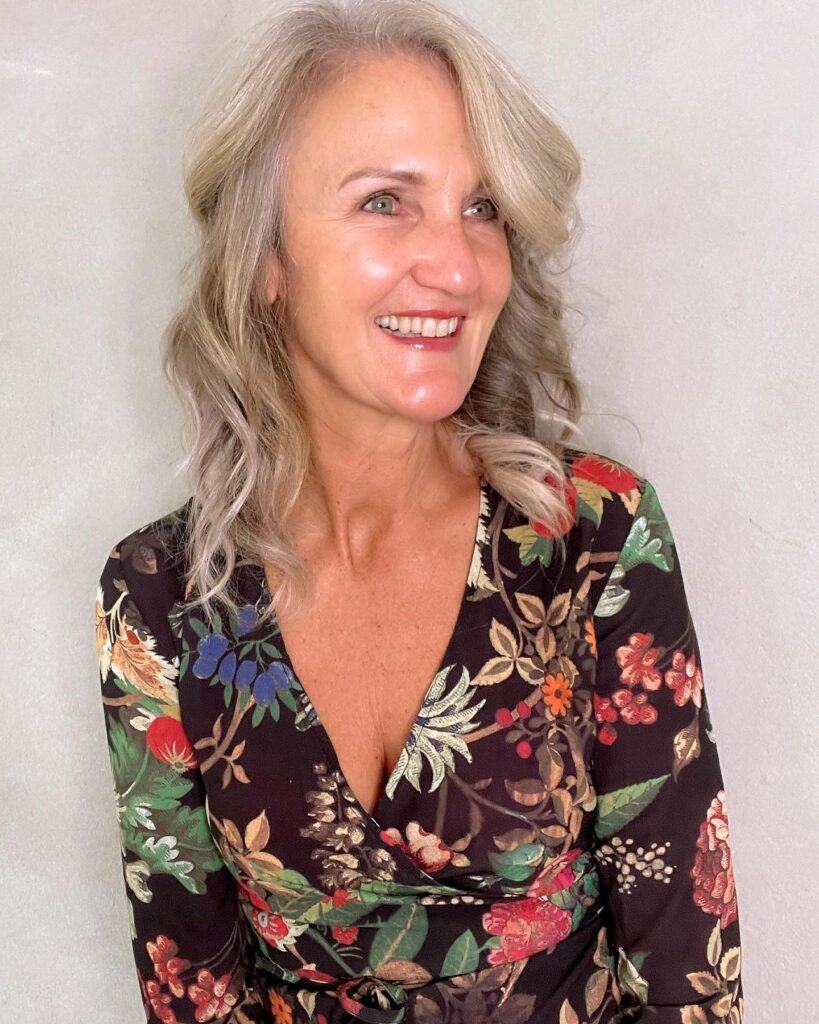 A smiling woman with shoulder-length champagne-blonde hair styled in loose beachy waves with a side part.