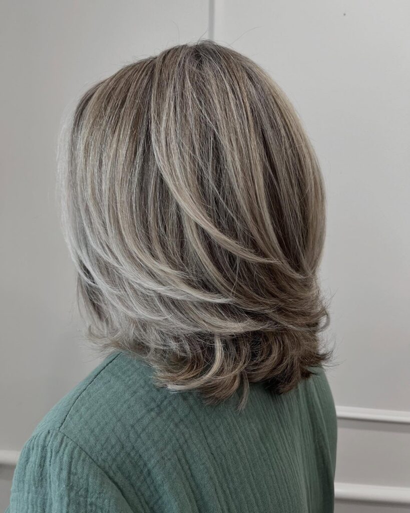 A woman with a shoulder-length ash brown lob featuring light silver highlights and soft internal layers.