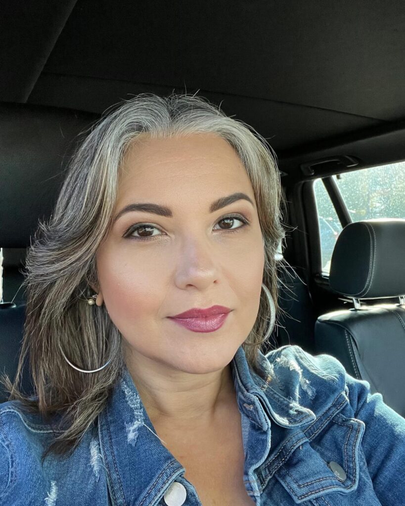 A woman with medium-length layered hair featuring natural silver highlights and soft outward-flipped ends.