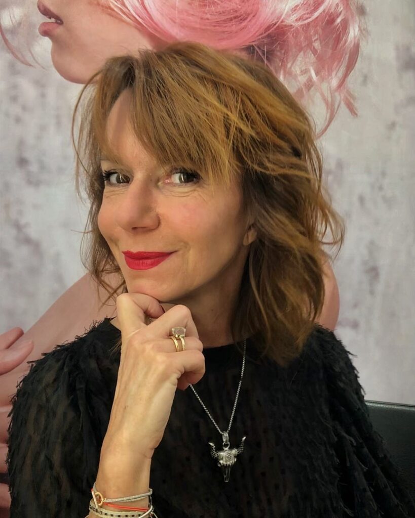 A woman with medium-length golden brown hair styled in soft, tousled waves with side-swept bangs.