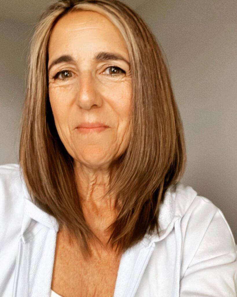 A woman with a straight shoulder-length brunette lob featuring a prominent silver streak at the front.