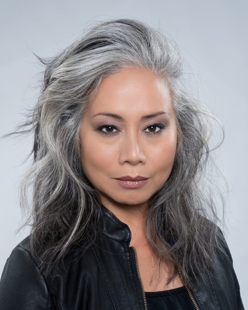A woman with textured medium-length salt-and-pepper hair featuring voluminous choppy layers and a tousled finish.