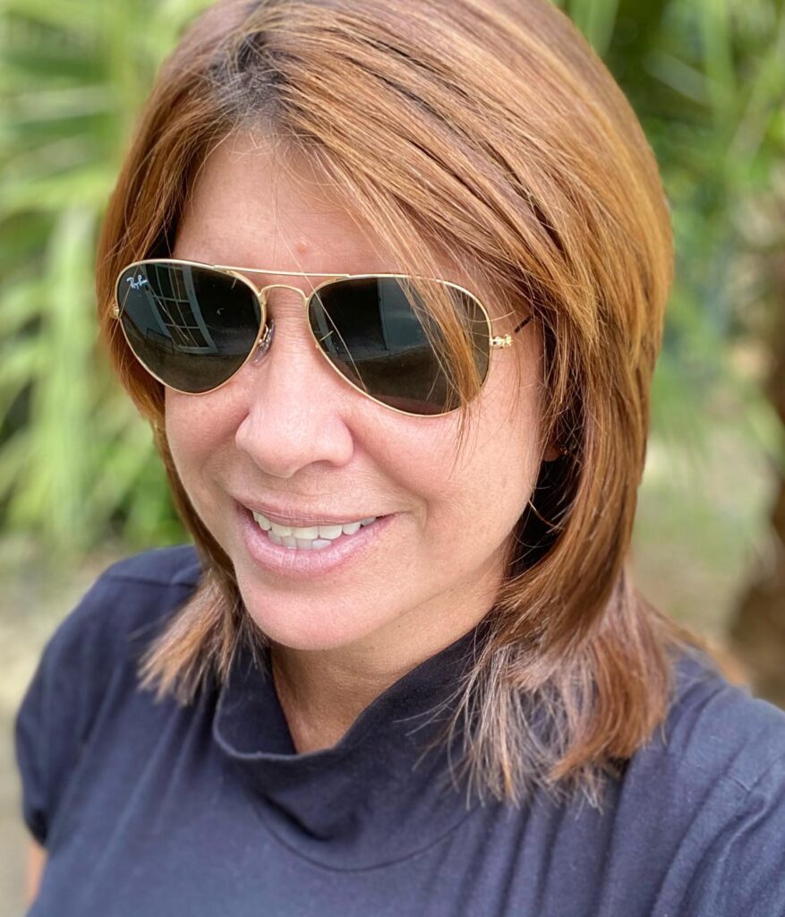 A woman wearing sunglasses with medium-length honey blonde hair styled in a layered long bob with side-swept bangs.