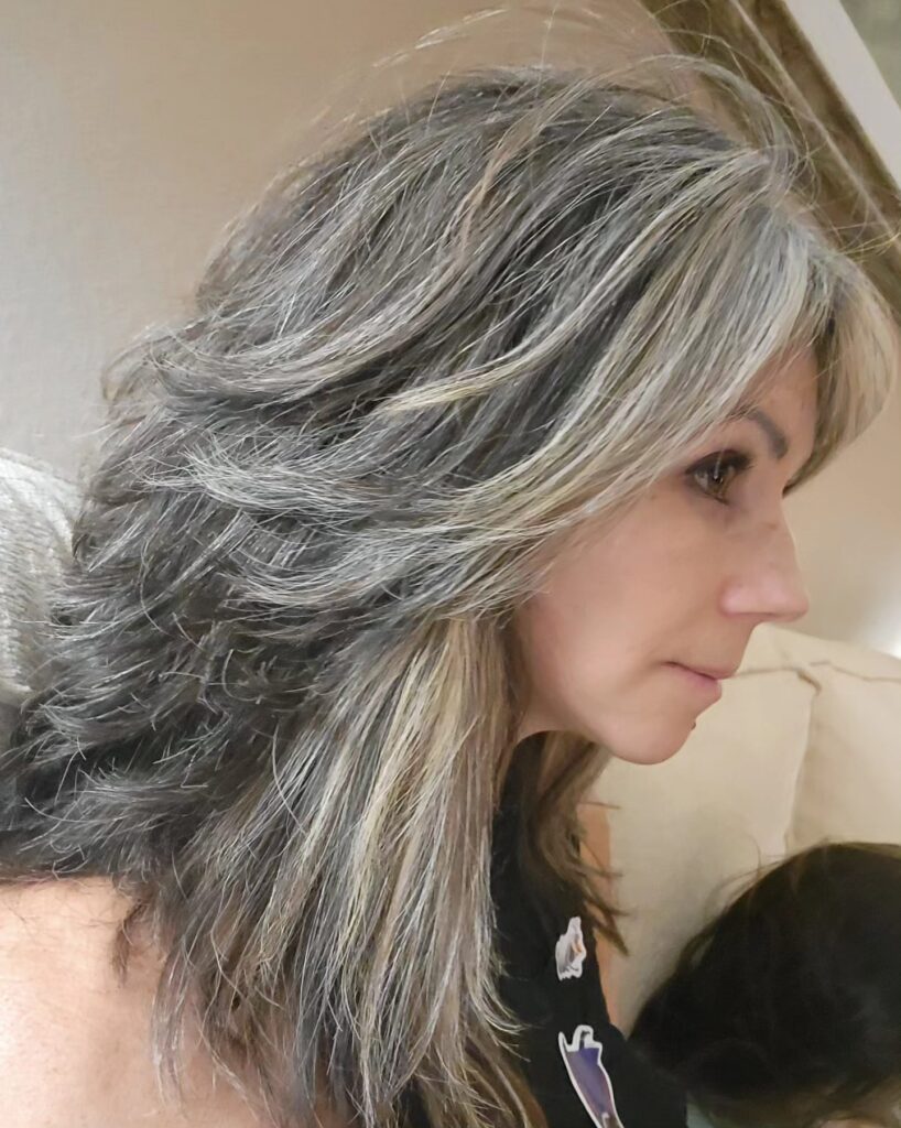 A woman with a shoulder-length feathered hairstyle featuring silver and blonde highlights and textured layers.