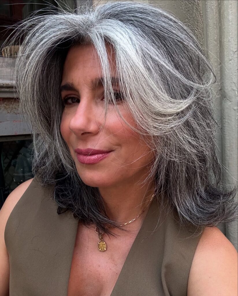A woman with a medium-length layered shag hairstyle featuring bold silver sweeps over a dark charcoal base.
